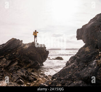 Woman wearing yellow rain jacket standing on rock Stock Photo