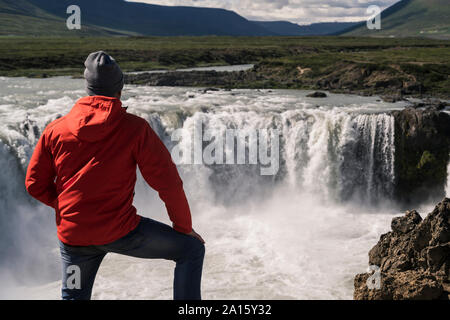 Man looking at Godafoss waterfalls, Iceland, with binoculars Stock Photo