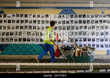 Hung Hau, Hong Kong. September 24  2019. A street sweeper walks by a Lennon Wall in Hung Hau.  This is one of many Lennon Walls containing posters, messages and grafitti that are found around Hong Kong. Stock Photo