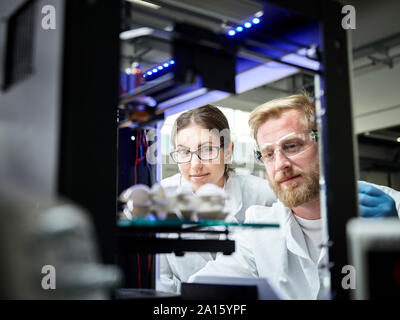 Two technicians looking at turbine wheel being printed in 3d printer Stock Photo