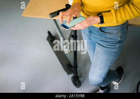 Young woman with e-scooter, using smartphone, close up Stock Photo
