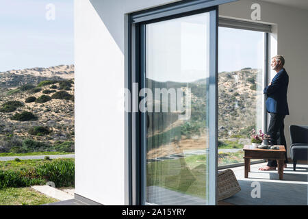 Senior businessman standing at panorama window looking out Stock Photo