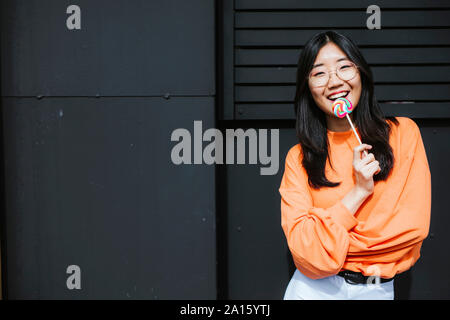 Young asian woman with lollipop in front of black wall Stock Photo
