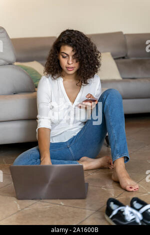 Young woman using cell phone and laptop at home Stock Photo