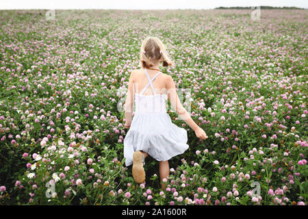 Rear view of a girl with braids running on clover field Stock Photo