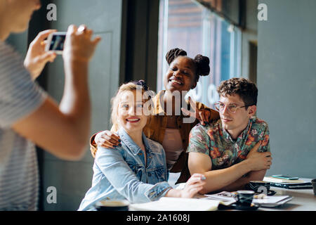 Students sitting in cafe, taking samrtphone selfies Stock Photo
