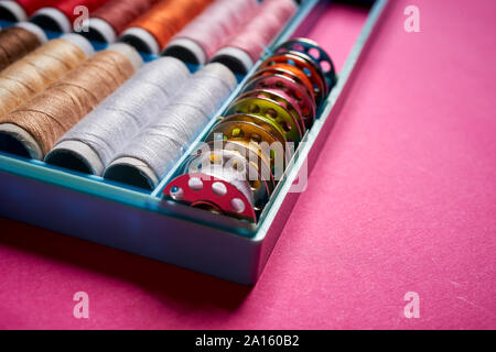 Close up of spools of colored threads in box on pink background Stock Photo