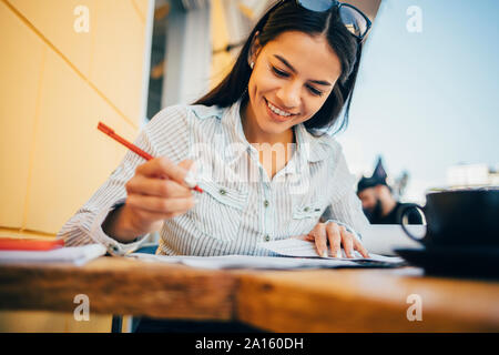 Smiling young woman taking notes in a cafe Stock Photo