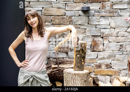 Portrait of confident woman with axe and firewood in front of a house Stock Photo