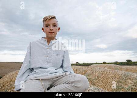 Portrait of blond boy, sitting on a hay bale Stock Photo