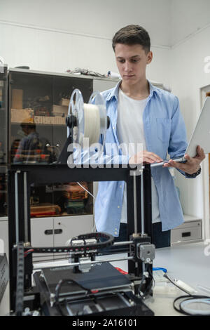 Student setting up 3D printer, using laptop Stock Photo