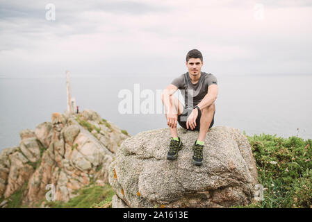 Portrait of trail runner sitting on a rock in coastal landscape, Ferrol, Spain Stock Photo