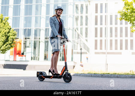Businesswoman wearing high heels riding electric scooter on the street Stock Photo