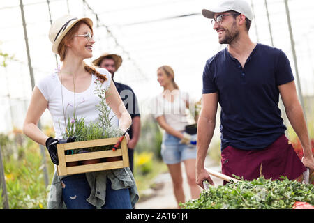 Smiling man and woman transporting plants with a wheelbarrow and wooden box in a greenhouse Stock Photo