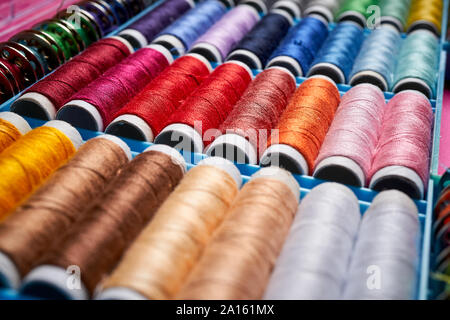 Close up of spools of colored threads in box on pink background Stock Photo