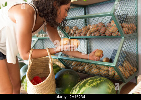 Young woman in organic store, choosing potatoes Stock Photo
