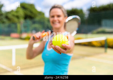 Smiling mature woman holding a tennis ball at tennis club Stock Photo