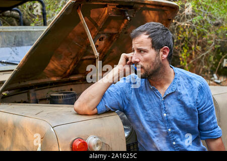Man at old car with open bonned calling a mechanic Stock Photo