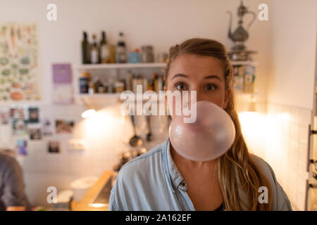 Young woman in kitchen at home making chewing gum bubble Stock Photo