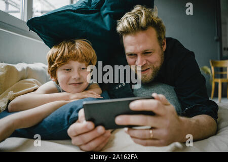 Portrait of father and son lying on couch looking at cell phone Stock Photo
