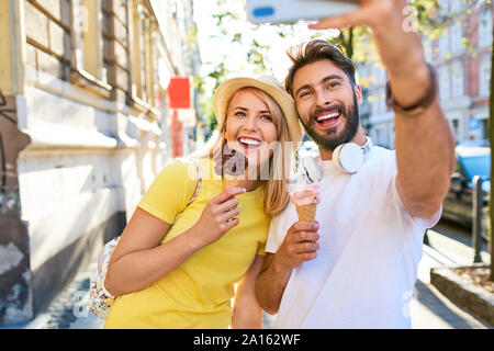 Happy young couple taking a selfie while eating ice cream in the city Stock Photo