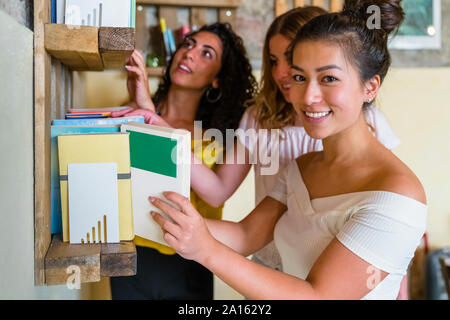 Three smiling young women at a bookshelf Stock Photo