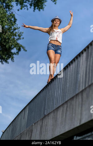 Smiling young woman balancing on a bridge railing Stock Photo