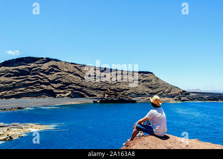 Man sitting on cliff looking towards El Golfo beach, Lanzarote, Canary Islands, Spain Stock Photo