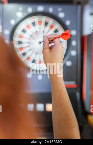 Close-up of woman's hand holding dart in front of dartboard Stock Photo