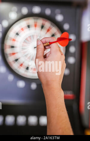 Close-up of woman's hand holding dart in front of dartboard Stock Photo