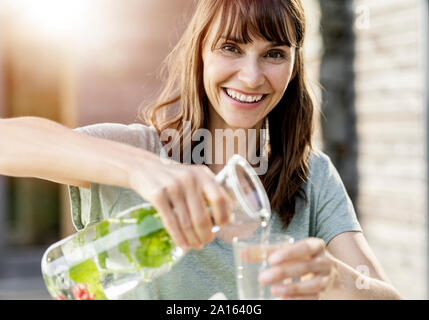 Portrait of happy woman pouring infused water into glass Stock Photo