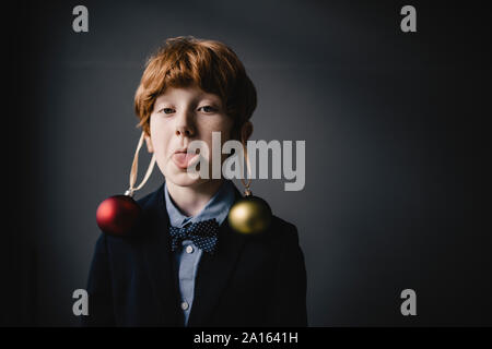Portrait of redheaded boy wearing bow tie and Christmas baubles sticking out tongue Stock Photo
