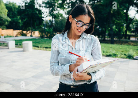 Smiling young businesswoman taking notes outdoors Stock Photo