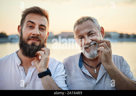 Portrait of smiling father and adult son scratching their beards Stock Photo