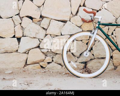 Fixie bike leaning against natural stone wall, partial view Stock Photo