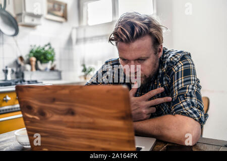 Man using laptop on kitchen table Stock Photo