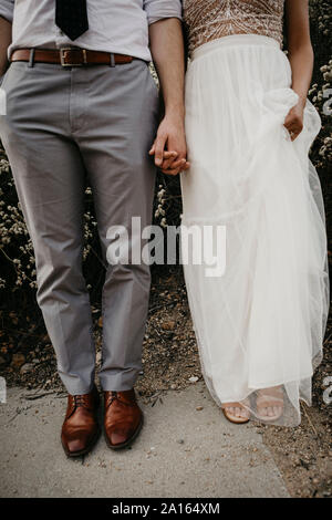 Low section of bride and groom holding hands outdoors Stock Photo