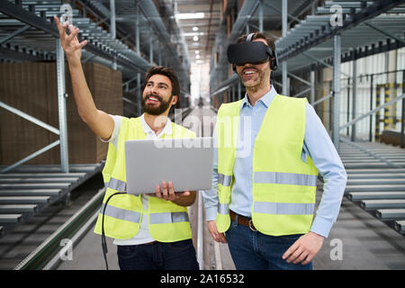 Man with laptop and businessman wearing VR glasses in factory Stock Photo