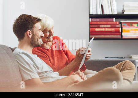 Grandson sitting on couch, using digital tablet with his grandmother Stock Photo