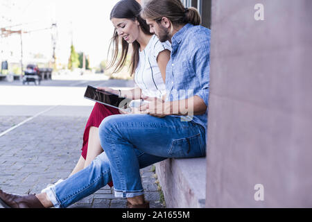 Young couple sitting on windowsill at a building using a tablet Stock Photo
