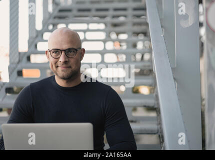 Portrait of bald man sitting on stairs using laptop Stock Photo