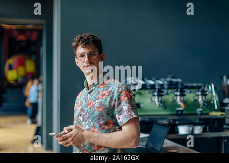 Young man standing in cafe, using smartphone Stock Photo