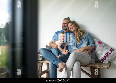 Happy family of three sitting on a bench at home Stock Photo