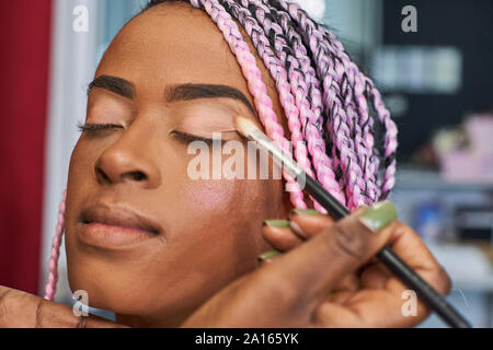 Visagiste applying eyeshadow on young woman's eyelid, close-up Stock Photo