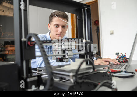 Student setting up 3D printer, using laptop Stock Photo