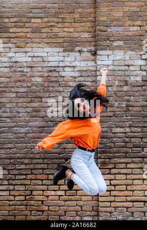 Asian woman jumping, brick wall in the background