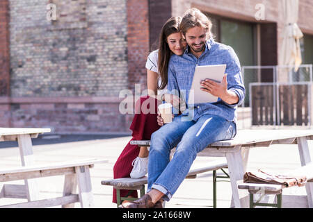 Young couple sitting on table in a beer garden looking at tablet Stock Photo