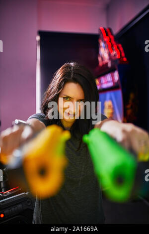 Portrait of smiling woman shooting with pistols in an amusement arcade Stock Photo