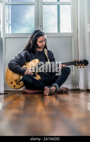 Young woman sitting on the floor at home playing guitar Stock Photo