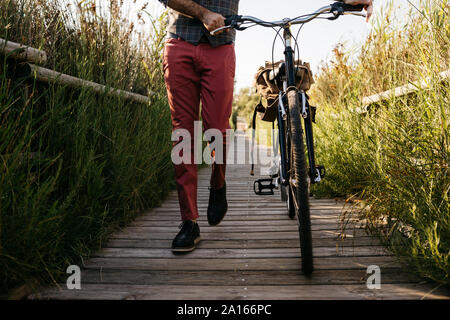 Well dressed man walking with his bike on a wooden walkway in the countryside after work Stock Photo